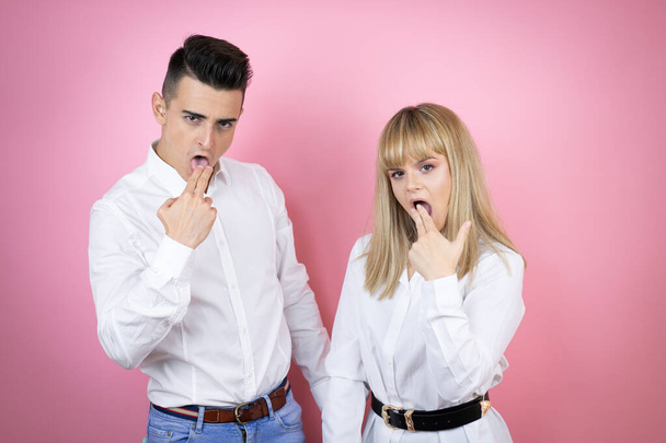 Young couple of girlfriend and boyfriend over isolated pink background disgusted with her hand inside her mouth - Photo, Image