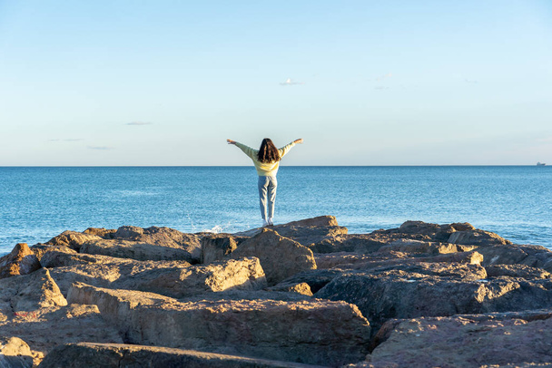 A female with open arms standing on rocky beach in Benicasim, Spain - Φωτογραφία, εικόνα