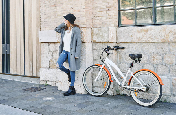 A Portrait young pretty Caucasian girl, in casual clothes, against the wall with a bike for a ride - Foto, imagen