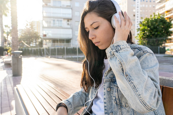 A selective focus shot of an attractive female in headphones sitting on a bench - Photo, Image