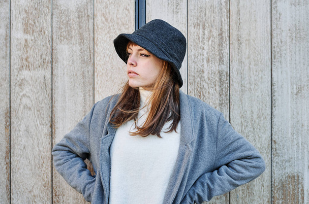 A Portrait young pretty Caucasian curious girl, dressed in a gray jacket, a white sweater and a hat. - Foto, afbeelding