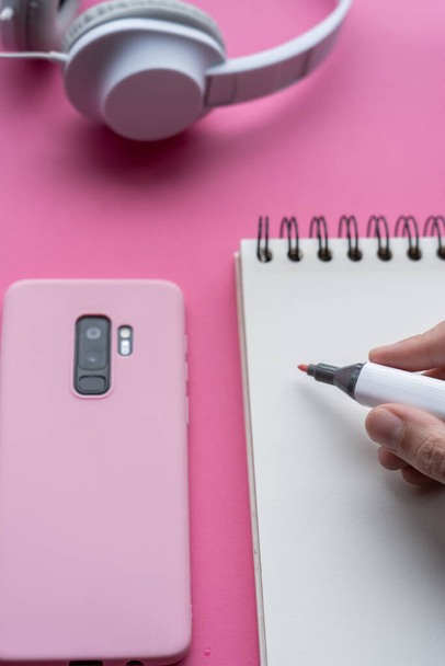 A vertic shot of a cellphone, headphones, and writing tools on a pink surface - Photo, image