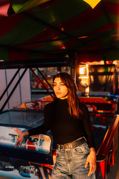 A beautiful Caucasian girl wearing a black turtleneck and posing in the amusement park - Фото, изображение