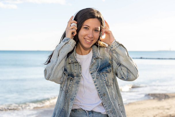 A selective focus shot of an attractive happy female in headphones enjoying music on a beach - Photo, image