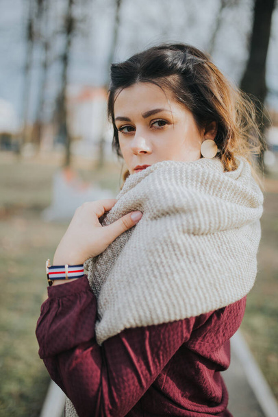 A portrait of a brunette young lady with a scarf and a coat smilingat the park at the fall - Фото, изображение