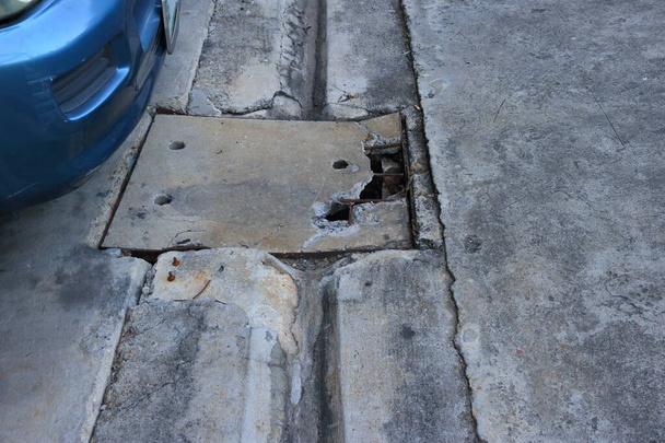Fechar a tampa danificada do dreno ao lado do estacionamento, um carro está estacionado perto do dreno  - Foto, Imagem