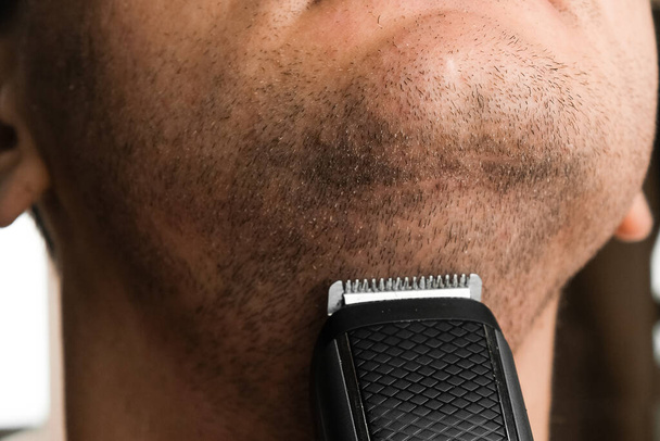 Ο άνθρωπος ξυρίζει το κοντό του γένι. Ερεθισμός μετά από την έννοια του ξυρίσματος με ηλεκτρικό ξυράφι.  - Φωτογραφία, εικόνα