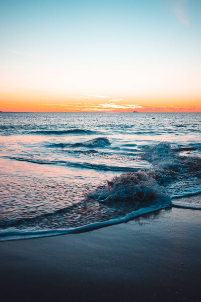 A vertical shot of an ocean and the seashore under a sunset sky - Photo, image