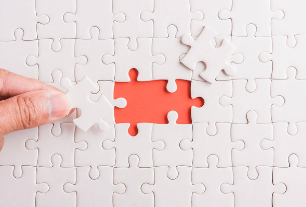 Top view flat lay of hand-holding last piece white paper jigsaw puzzle game last pieces put to place for solve problem complete mission, studio shot on a pink background, quiz calculation concept - Photo, Image