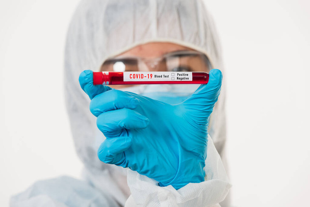 Medical scientist in PPE uniform wear a mask holding test tube Coronavirus test blood sample in a hospital laboratory for analyzing isolated on white, medicine COVID-19 pandemic outbreak concept - Foto, imagen
