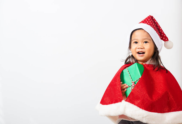 Kid dressed in red Santa Claus hat hold gift box on hands, Asian little child cute girl smile and exciting concept of holiday Christmas Xmas day or Happy new year isolated on white background - Foto, imagen