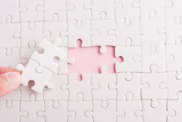 Top view flat lay of hand-holding last piece white paper jigsaw puzzle game last pieces put to place for solve problem complete mission, studio shot on a pink background, quiz calculation concept - 写真・画像