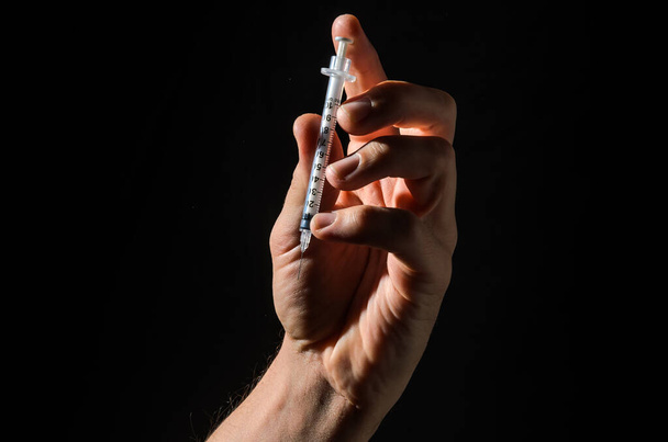 Hand with injection syringe on black background - Foto, afbeelding
