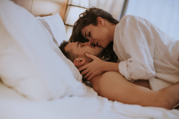 Красивая молодая любящая пара лежит на кровати в комнате - Фото, изображение