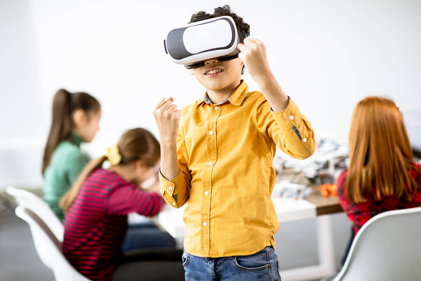 Lindo niño pequeño con gafas de realidad virtual VR en un aula de robótica - Foto, Imagen