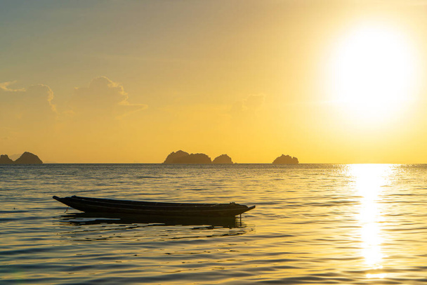 Beautiful sunset on the coast of a tropical island in Thailand, a silhouette of a boat in the ocean. - Фото, изображение