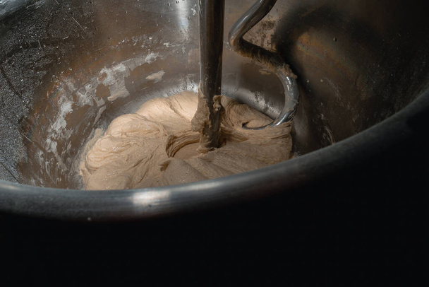 Il processo di fabbricazione di prodotti da forno di pane. Impastare la pasta, la farina e l'acqua. Miscelatore industriale, automatico. La vista è vicina. Copia spazio - Foto, immagini