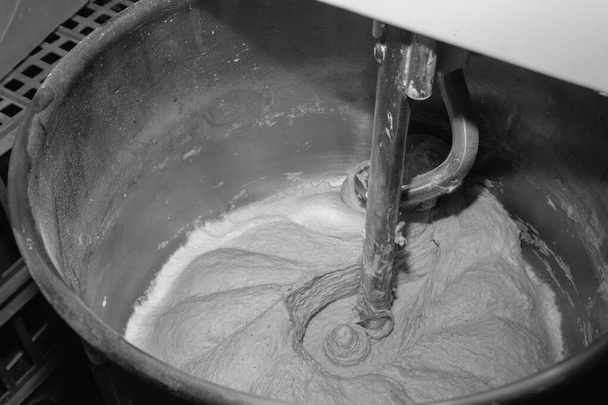 Der Prozess der Herstellung von Brotbackwaren. Teig, Mehl und Wasser kneten. Industriemaschine, automatisch. Der Blick ist nah. Schwarz-Weiß - Foto, Bild