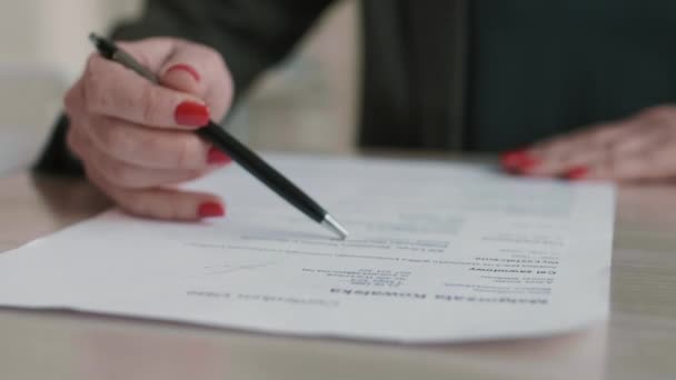 Nahaufnahme einer unkenntlichen Person mit Händen mit rotem Polster auf Nägeln, die einen Stift in der Hand halten und ihn über Dokument auf Schreibtisch schieben - Filmmaterial, Video