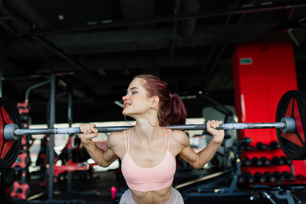 Chica atlética en ropa deportiva realiza ejercicios con una barra, mancuernas. Fitness, entrenamiento, estilo de vida saludable - Foto, imagen