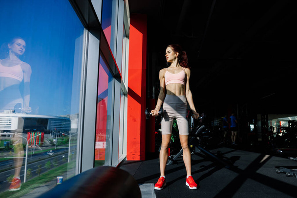 Menina atlética em sportswear executa exercícios com um sino de barra, halteres. Fitness, treino, estilo de vida saudável - Foto, Imagem