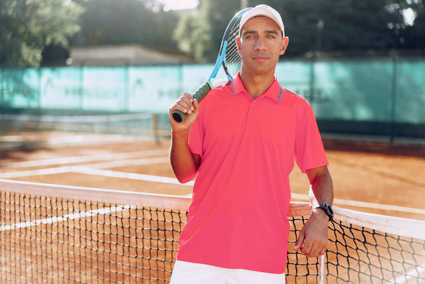 Middle-aged man tennis player with racket standing on court near net - Zdjęcie, obraz