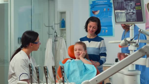 Bambino usando il dito per puntare il dente colpito mentre il dentista parla con la madre - Filmati, video