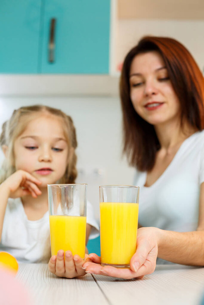 Mother with little girl drinking orange juice while they have breakfast together - Фото, зображення