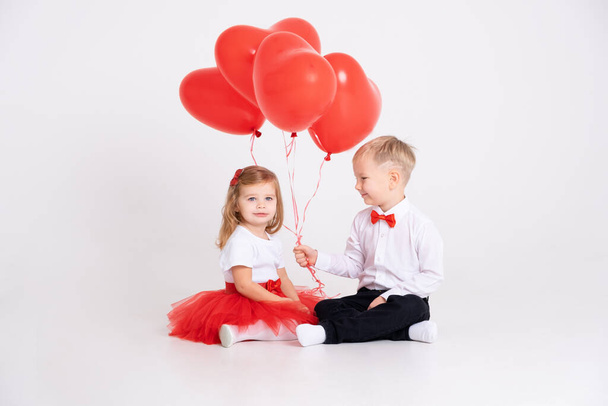 niño pequeño dando globos de corazón a niña en el día de San Valentín sobre fondo blanco - Foto, Imagen