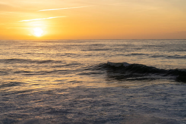 Beau coucher de soleil sur l'océan avec un ciel coloré et de grandes vagues roulant vers la côte - Photo, image