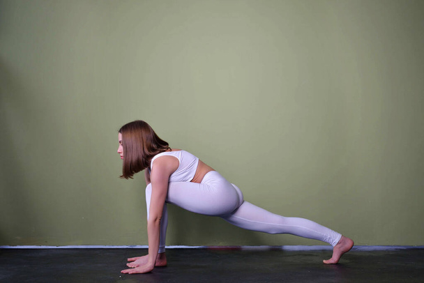Hermosa joven morena con ropa deportiva blanca practicando yoga, atractiva chica trabajando en un moderno estudio de yoga - Foto, Imagen