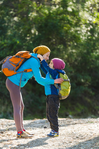 A boy with a backpack walks in the forest with his mom, the child hugs his mom, the woman travels with the child, mother's support, mother's day. - Foto, imagen