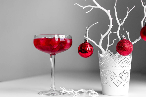Red Christmas balls on white branch on light and dark background. Red cocktail Margarita fresh in a martini glass with sparkling wine.  Merry Cristmas greeting card with Christmas decoration.  - Фото, изображение