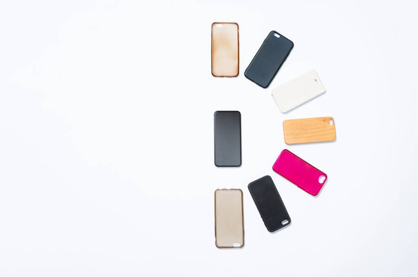 Stapel veelkleurige plastic achterhoezen voor mobiele telefoon op witte achtergrond. Keuze uit accessoires voor smartphonebeschermers. Veel siliconen telefoon rug of huiden naast de smartphone - Foto, afbeelding
