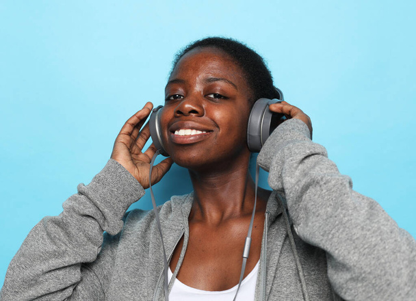 Adorable american woman singing and having fun while listening to music using headphones isolated over blue background. Lifestyle. - Foto, immagini