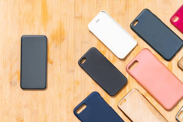 Stapel veelkleurige plastic achterhoezen voor mobiele telefoons op houten ondergrond met een telefoon aan de zijkant - Foto, afbeelding