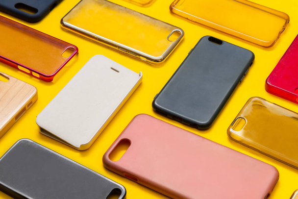 Pile of multicolored plastic back covers for mobile phone. Choice of smart phone protector accessories on yellow background. A lot of silicone phone backs or skins next to each other - Foto, Bild