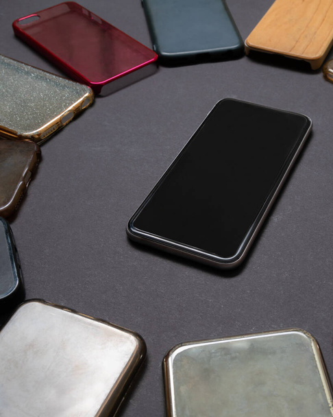 Stapel von mehrfarbigen Plastikrückdeckeln für Mobiltelefone auf schwarzem Hintergrund mit einem Telefon an der Seite - Foto, Bild