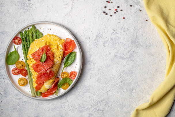 Fried eggs with green asparagus and salmon, cherry tomatoes and fresh spinach. Omelet with filling for breakfast. Healthy or ketogenic or no carbohydrate food concept. - 写真・画像