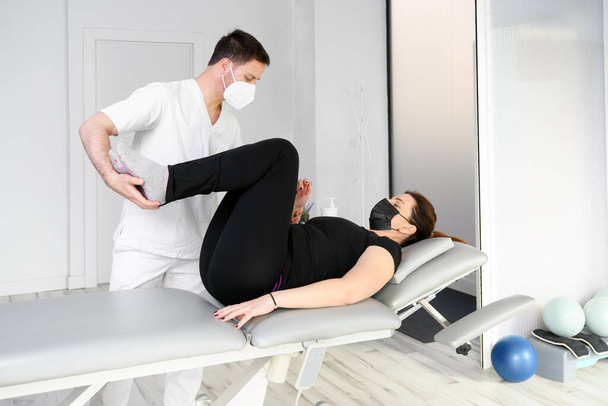 Physiotherapeut mit Schutzmaske, der einem Patienten eine Massage verabreicht. Wiedereröffnung mit physiotherapeutischen Sicherheitsmaßnahmen bei der Covid-19-Pandemie. Osteopathie, therapeutische Chiromassage - Foto, Bild