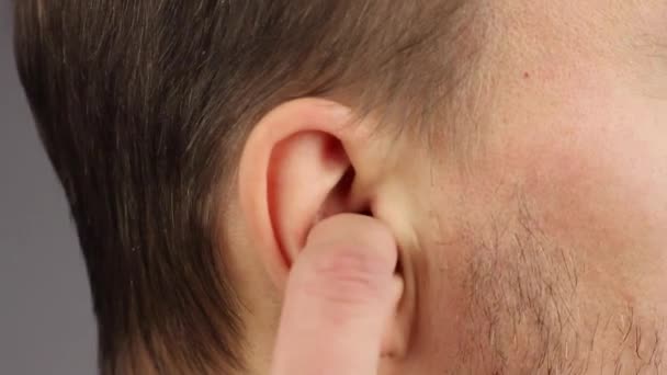 man picks his right ear with his index finger, loud noise or itch, personal hygiene, close-up, gray background, bad habit - Footage, Video