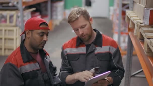 Medium footage of construction supervisor showing middle-eastern workman process of scanned barcodes on digital tablet standing among boxes at big warehouse - Footage, Video