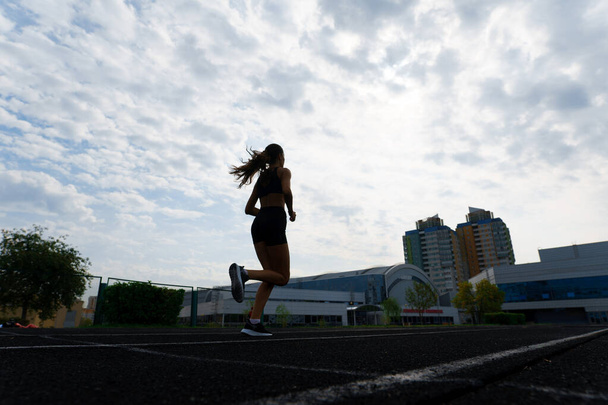 Athlete runner running on athletic track training her cardio. Woman jogging for competition race at summer outdoor stadium. - Foto, afbeelding