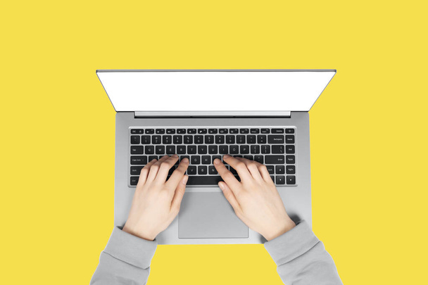 Person working on a laptop computer in a modern space. Female hands working on new laptop with blank screen isolated on illuminating yellow background. - Foto, imagen
