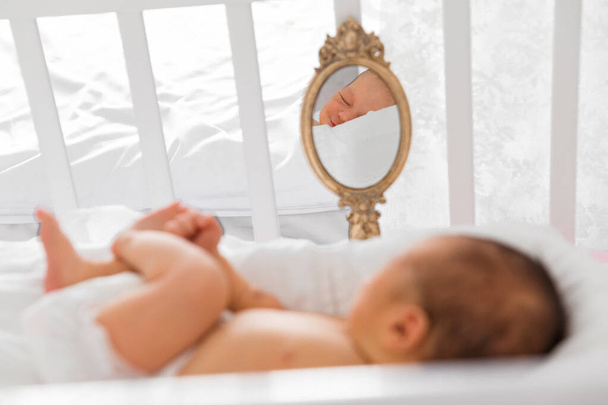 a newborn baby is lying in a crib and is reflected in a small mirror.  - Valokuva, kuva