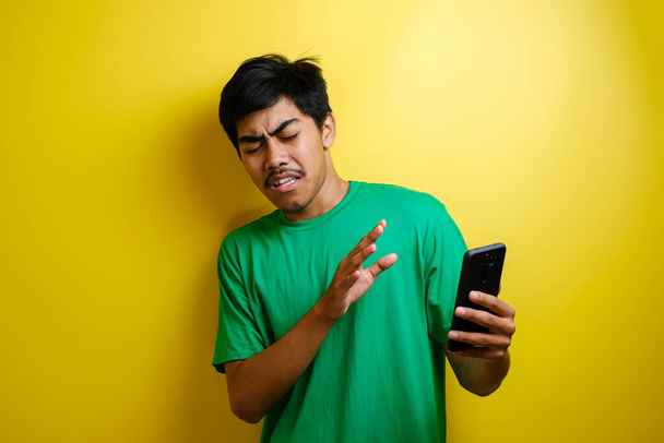 Atraente jovem asiático homem lendo mensagens de texto conversando em seu telefone, más notícias, triste chorando expressão contra fundo amarelo - Foto, Imagem