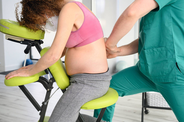 Fisioterapeuta masculino cura el dolor de espalda de una mujer embarazada. - Foto, imagen