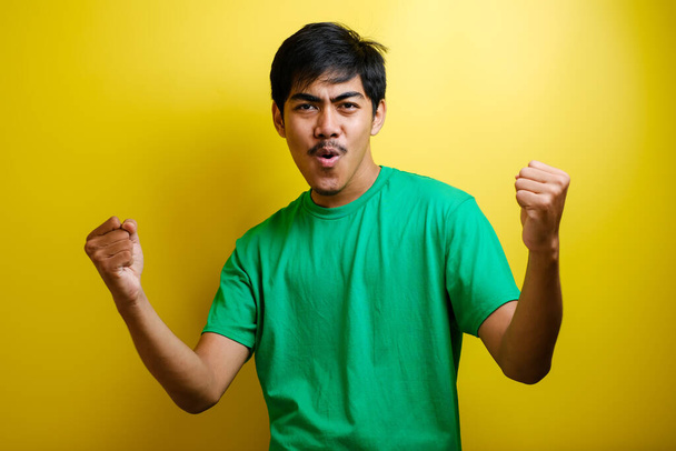 Задоволений молодим азіатом, який піднімає кулаки з усмішкою, радісним обличчям, так жестом, відзначаючи успіх на жовтому фоні. - Фото, зображення