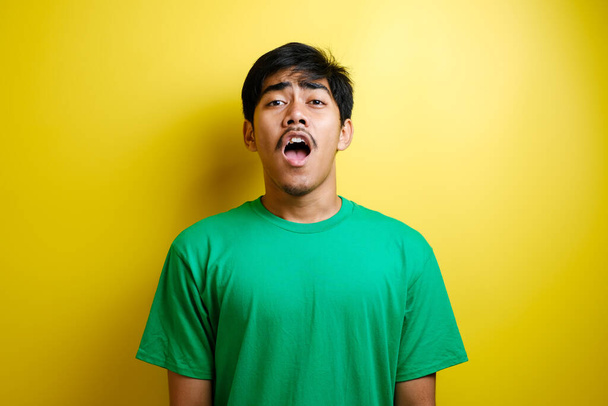 Geschokt gezicht van Aziatische man in groen t-shirt op gele achtergrond - Foto, afbeelding
