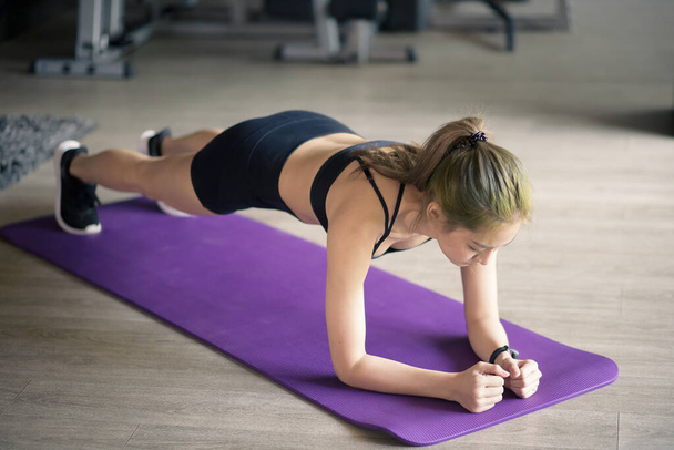 A happy beautiful woman is doing yoga plank on mat at the gym, concept of healthy lifestyle, sports, training, wellness, and sport.  - Photo, Image